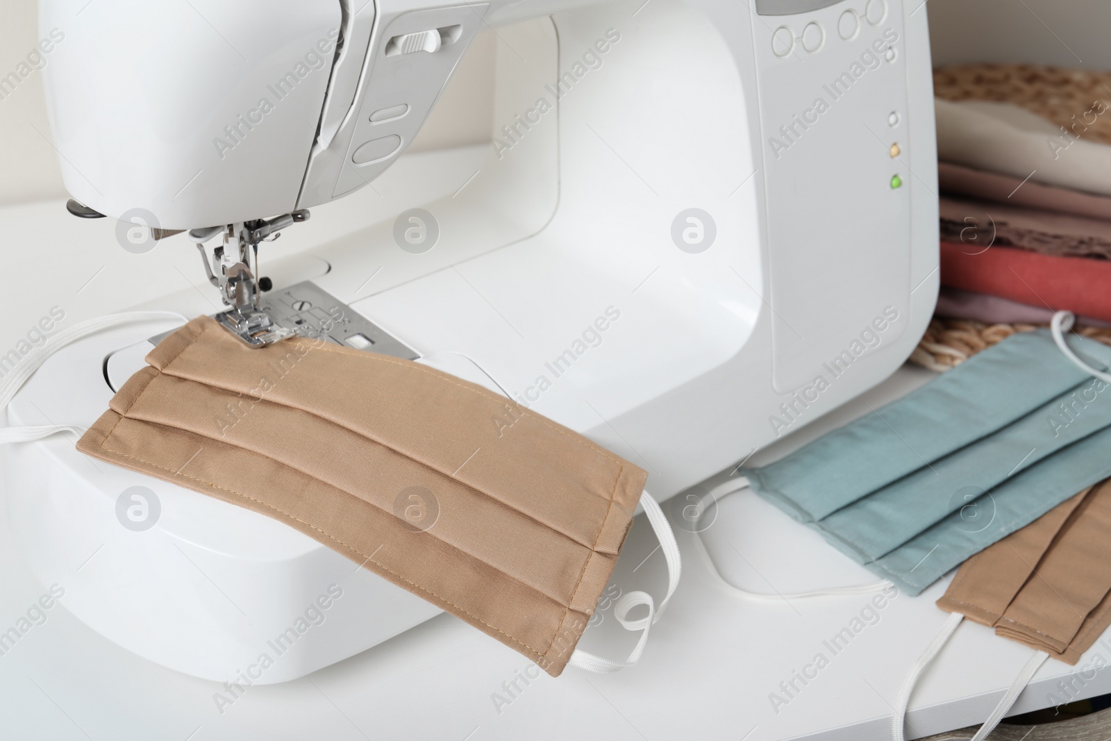 Photo of Sewing machine and homemade protective masks on white table