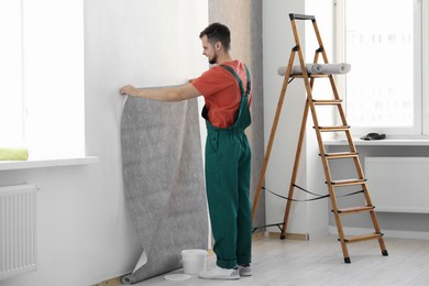 Man hanging stylish gray wallpaper in room