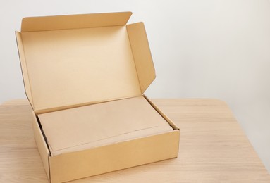 Photo of Open cardboard box with item wrapped in kraft paper on wooden table, space for text. Delivery service