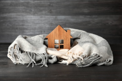 Photo of Wooden house model and scarf on grey table. Heating efficiency