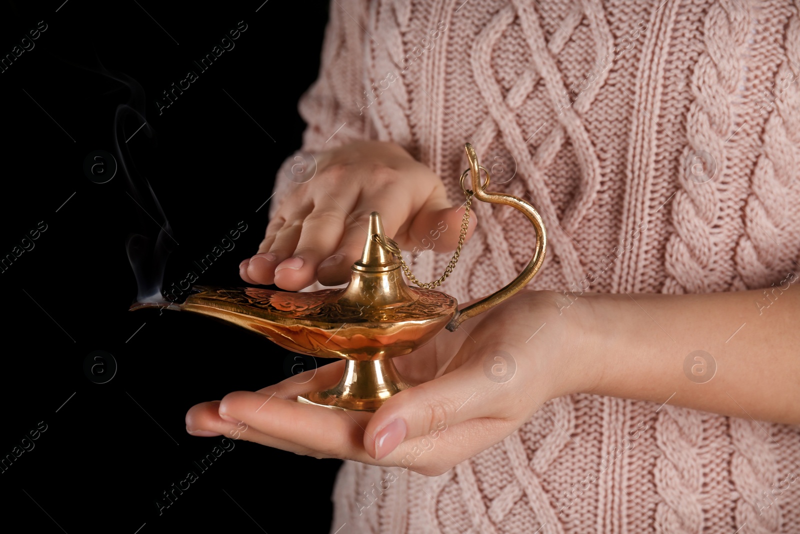 Photo of Young woman rubbing Aladdin magic lamp on black background, closeup