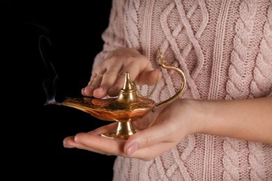 Young woman rubbing Aladdin magic lamp on black background, closeup