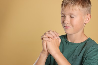 Photo of Boy with clasped hands praying on beige background, space for text