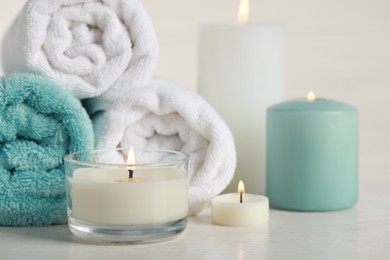 Photo of Beautiful spa composition with burning candles and rolled towels on white table, closeup
