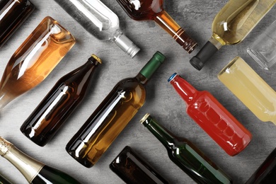 Photo of Bottles with different alcoholic drinks on grey background, flat lay