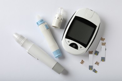 Photo of Digital glucometer, lancet pens and test strips on white background, flat lay. Diabetes control