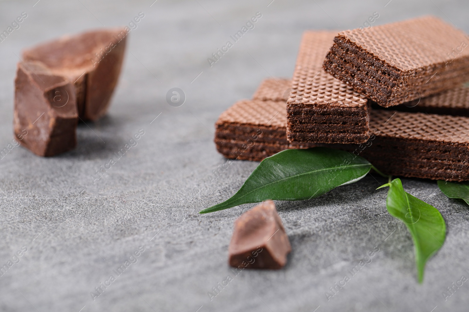 Photo of Delicious chocolate wafers with leaves on grey stone background