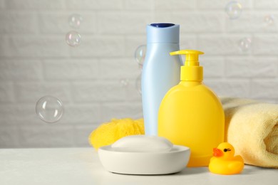 Baby cosmetic products, bath duck, sponge and towel on white table against soap bubbles. Space for text