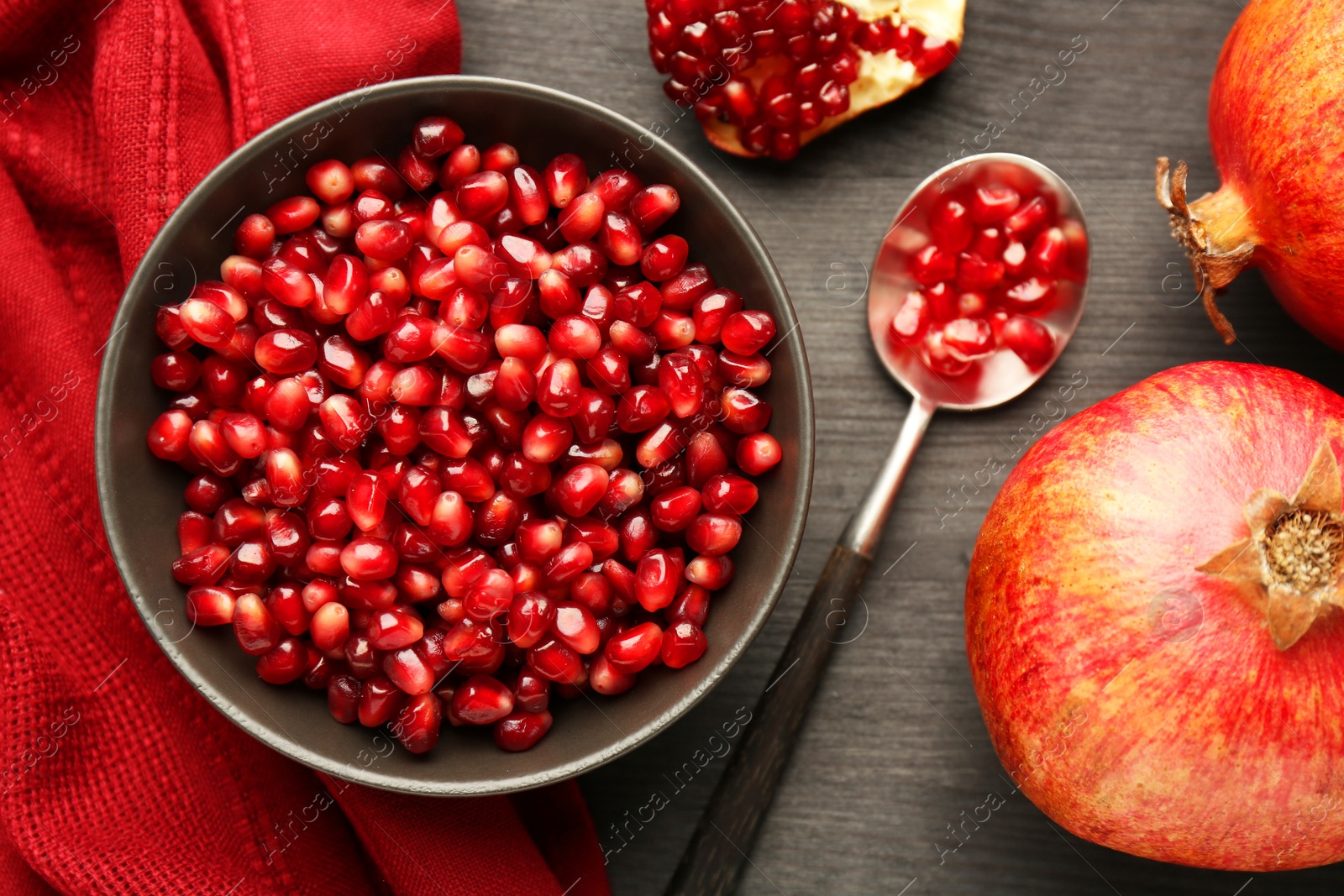 Photo of Tasty ripe pomegranates and grains on dark wooden table, flat lay