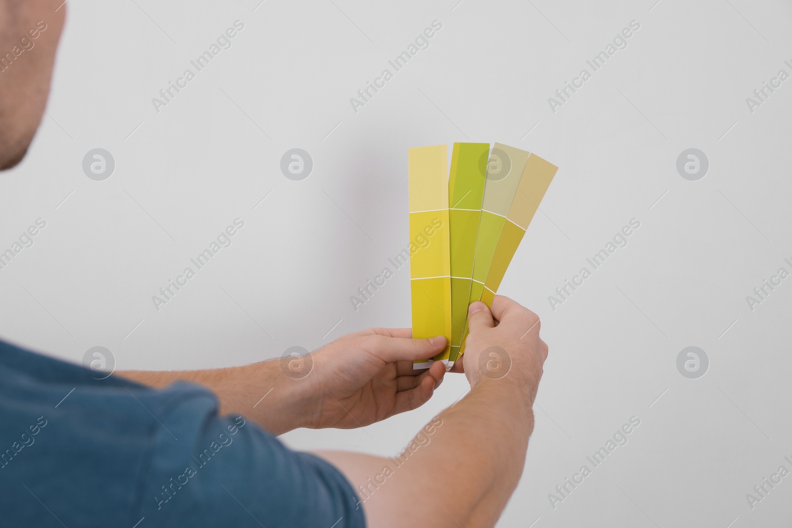 Photo of Man with palette choosing color for painting wall indoors, closeup. Interior design