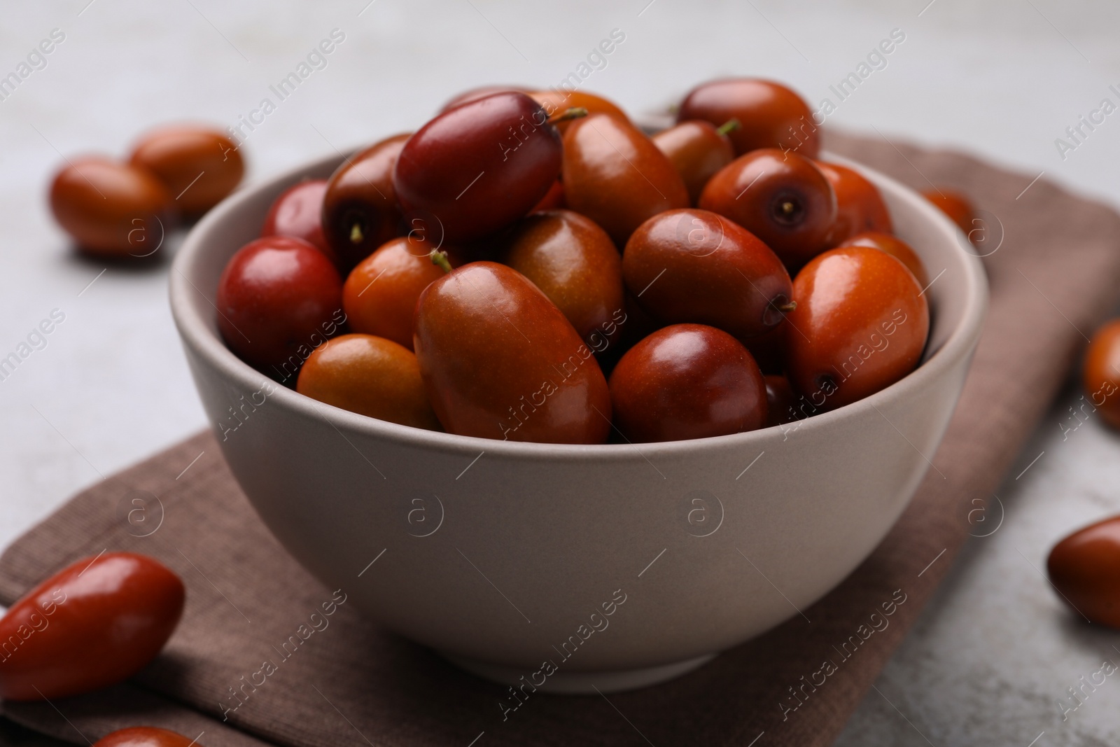 Photo of Fresh Ziziphus jujuba fruits with bowl and napkin on table, closeup