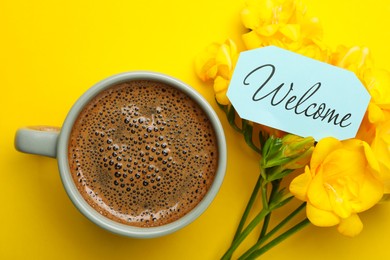 Welcome card, beautiful freesia flowers and cup of aromatic coffee on yellow background, flat lay