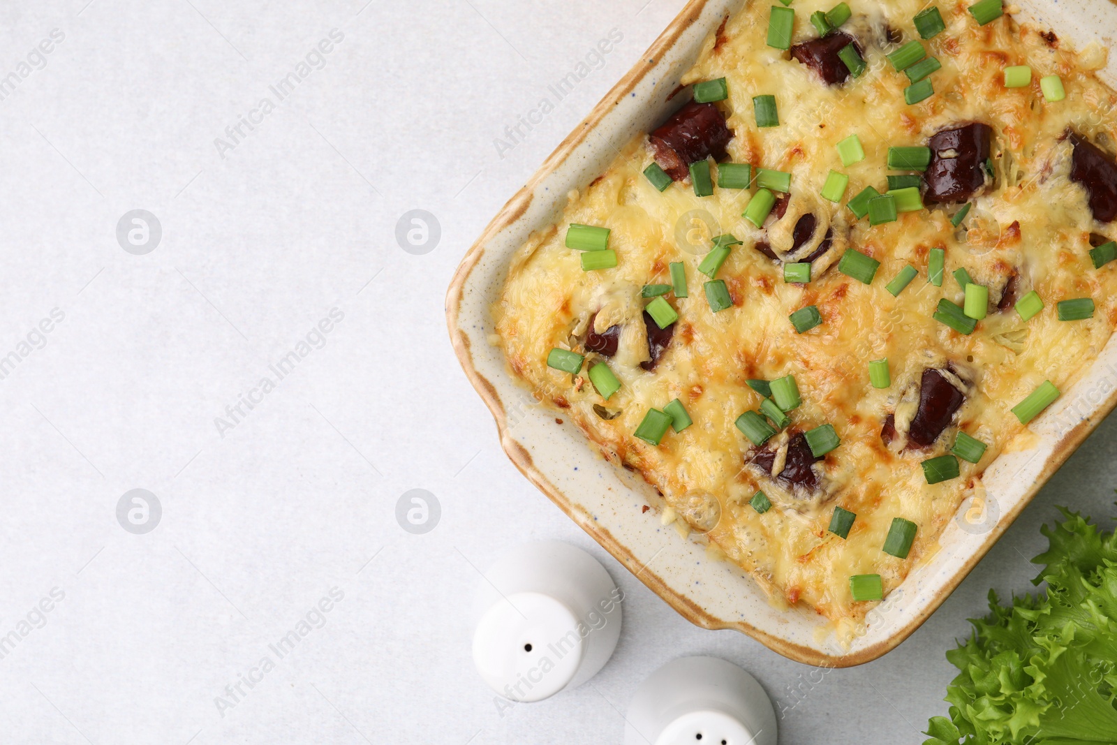 Photo of Tasty sausage casserole with green onions in baking dish served on white table, flat lay. Space for text