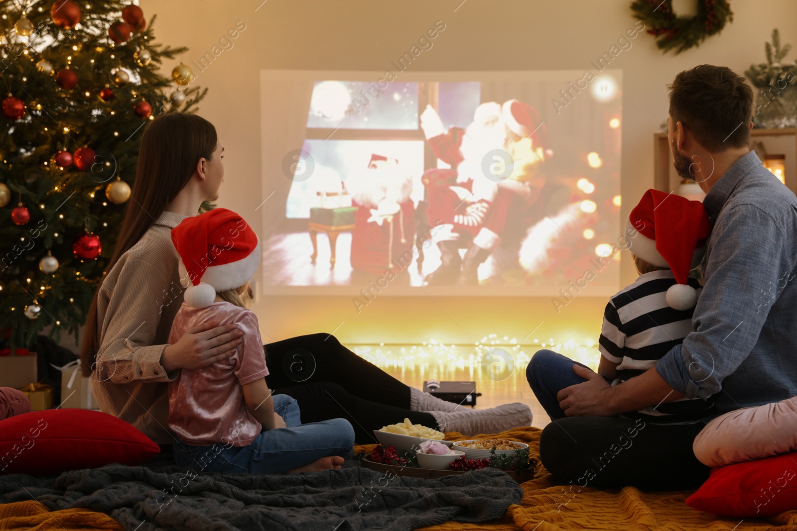 Photo of Family watching Christmas movie via video projector in cosy room. Winter holidays atmosphere