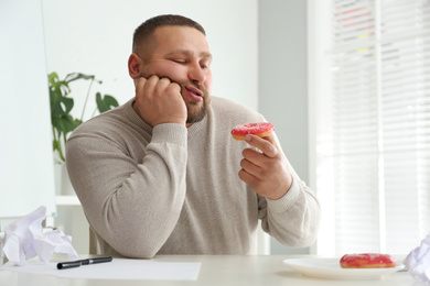 Photo of Lazy overweight office employee with donut at workplace