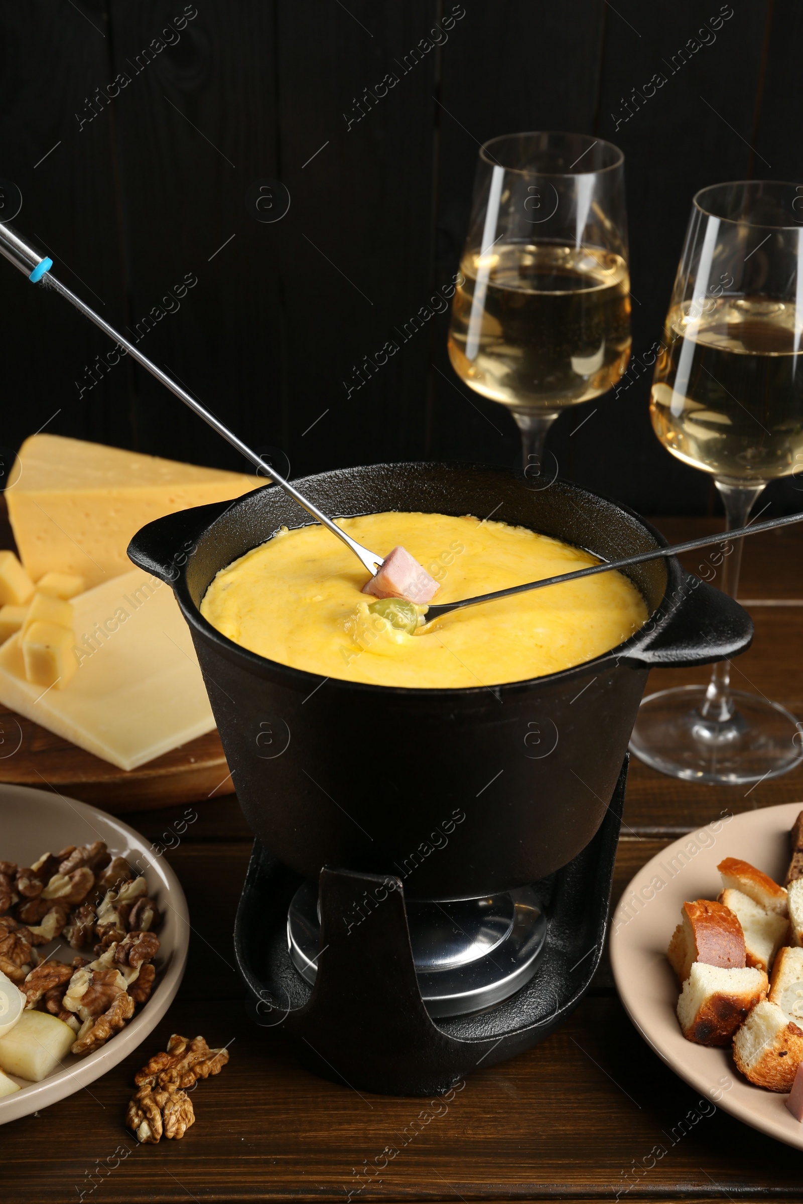 Photo of Fondue pot with melted cheese, glasses of wine, forks and different products on wooden table