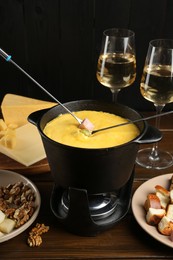 Fondue pot with melted cheese, glasses of wine, forks and different products on wooden table