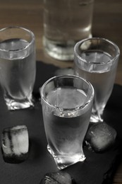 Photo of Shot glasses of vodka with ice cubes on table, closeup
