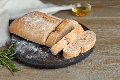 Photo of Cut delicious ciabatta with rosemary on wooden table