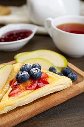 Fresh tasty puff pastry with jam, blueberries and pear on wooden table, closeup