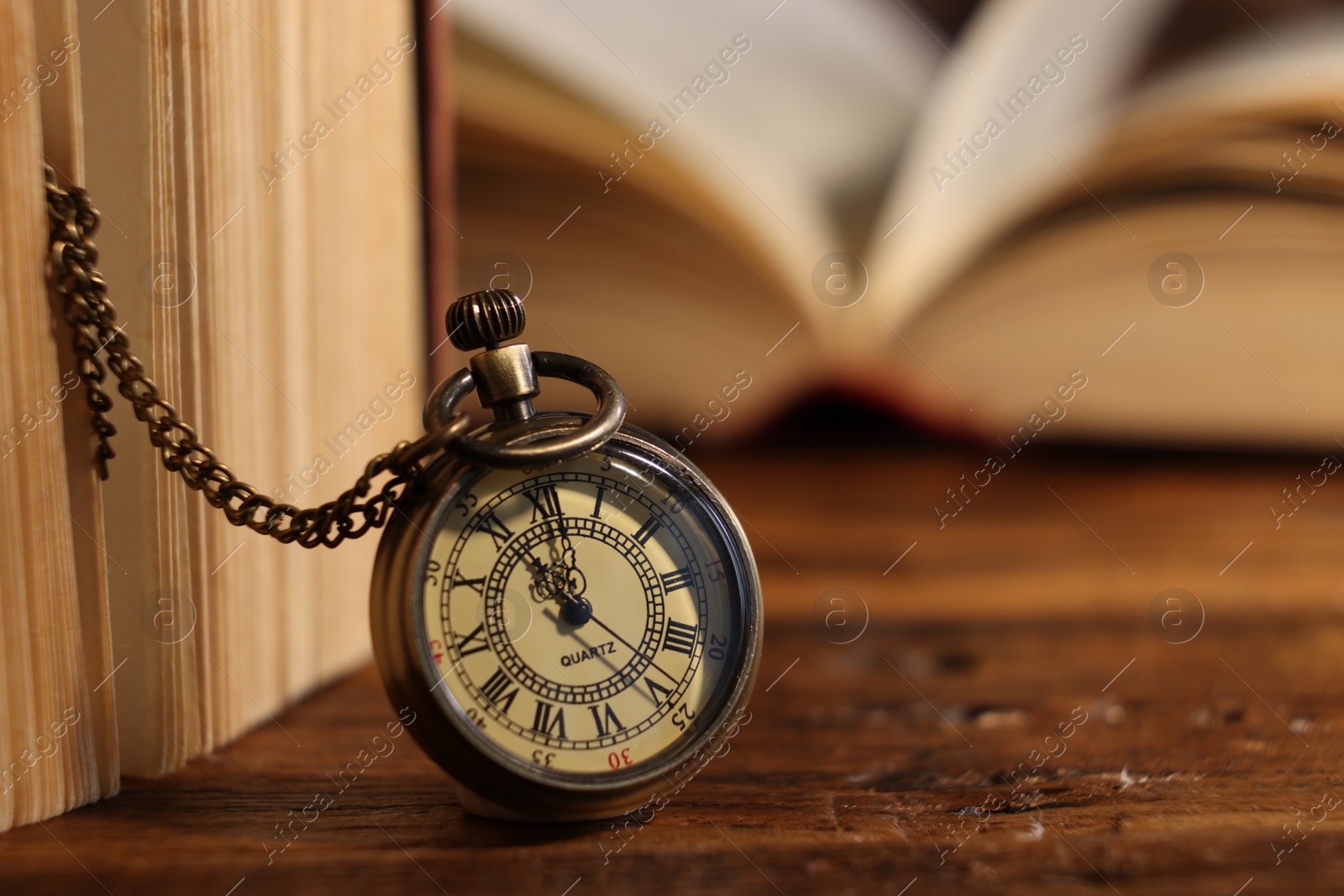 Photo of Pocket clock with chain and book on wooden table, closeup. Space for text