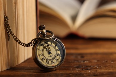 Pocket clock with chain and book on wooden table, closeup. Space for text