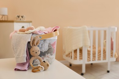 Photo of Laundry basket with baby clothes and crochet toys on white table in child room, space for text