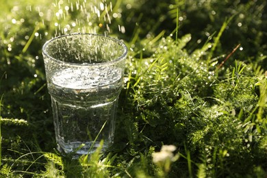 Photo of Glass of fresh water on green grass outdoors, closeup