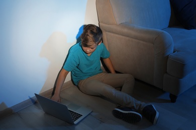 Photo of Little child with laptop on floor in dark room. Danger of internet