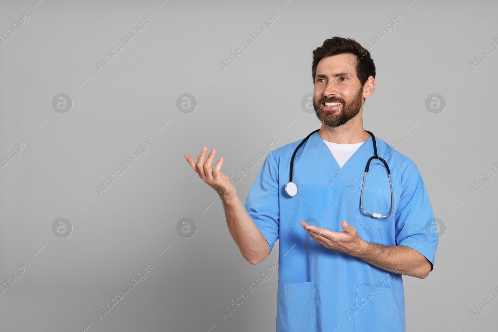 Photo of Happy doctor with stethoscope on light grey background. Space for text