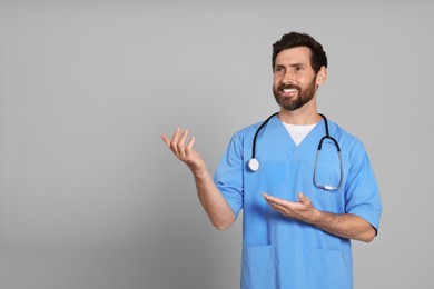 Photo of Happy doctor with stethoscope on light grey background. Space for text