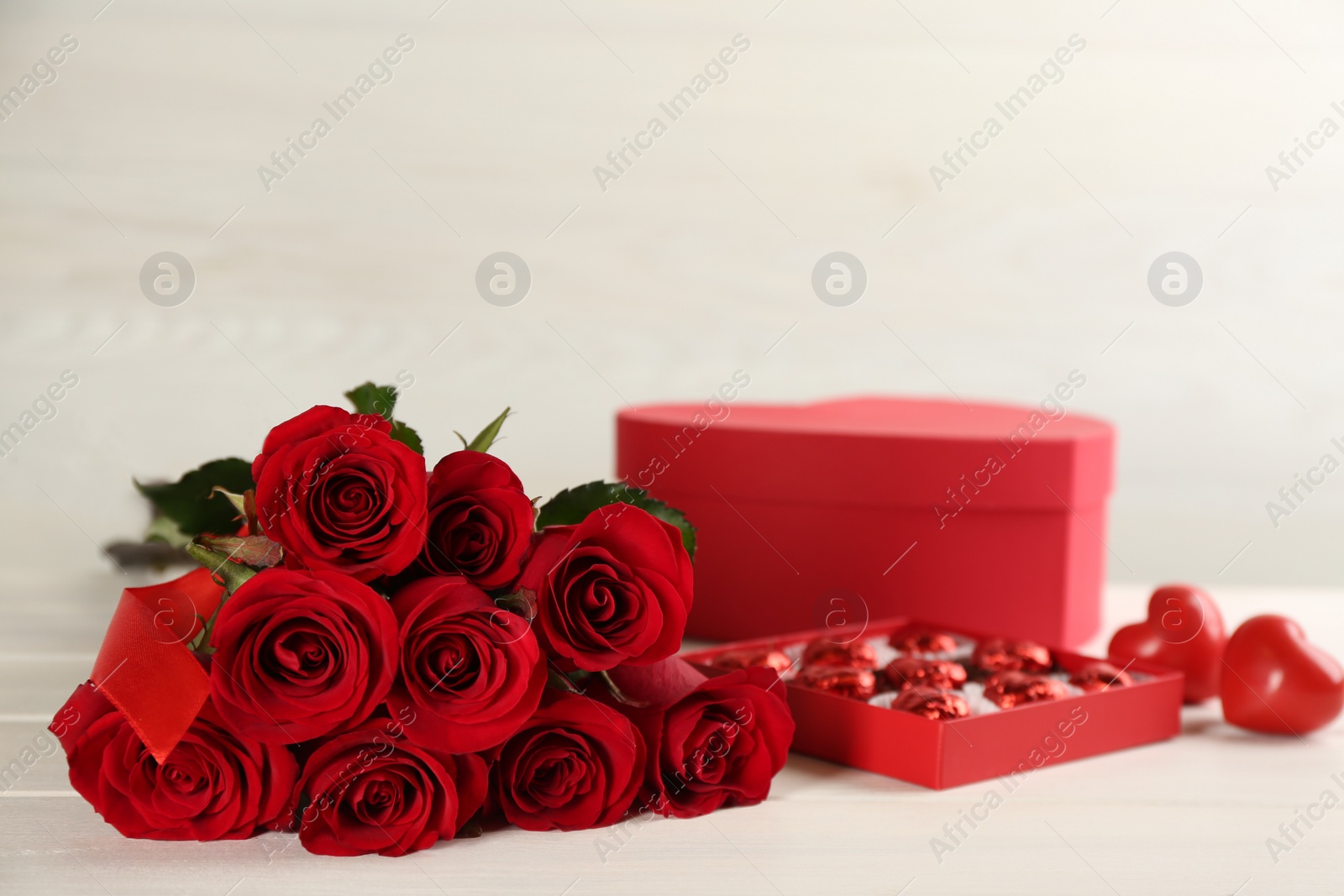 Photo of Beautiful red roses, sweet candies, decorative hearts and gift box on white table. St. Valentine's day celebration