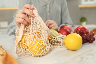 Photo of Woman with string bag of fresh fruits at light marble table, closeup