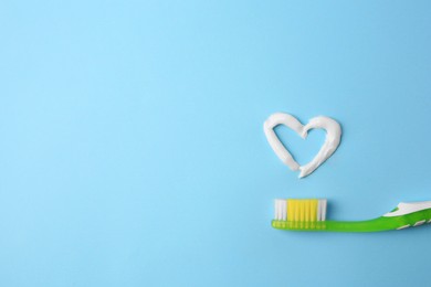 Photo of Heart made with toothpaste and brush on light blue background, top view. Space for text