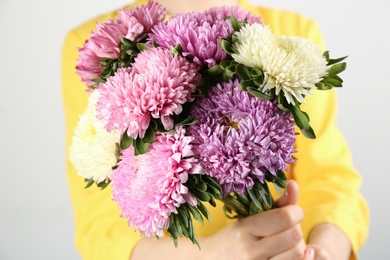 Photo of Woman with bouquet of beautiful asters on light background, closeup. Autumn flowers