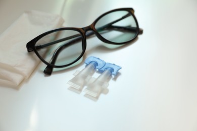 Photo of Single dose eye drops, glasses and fabric on white table