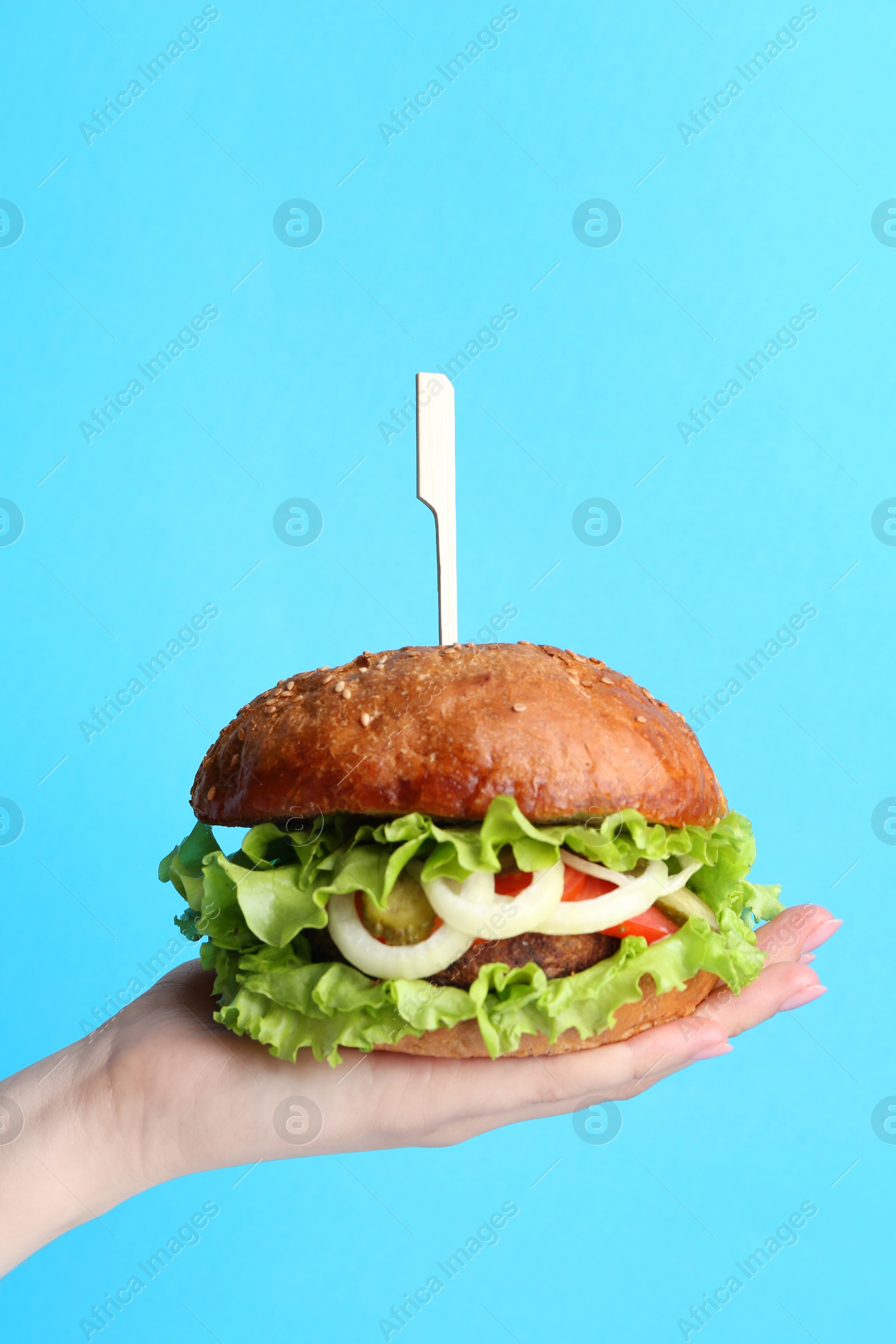 Photo of Woman holding delicious vegetarian burger on light blue background, closeup