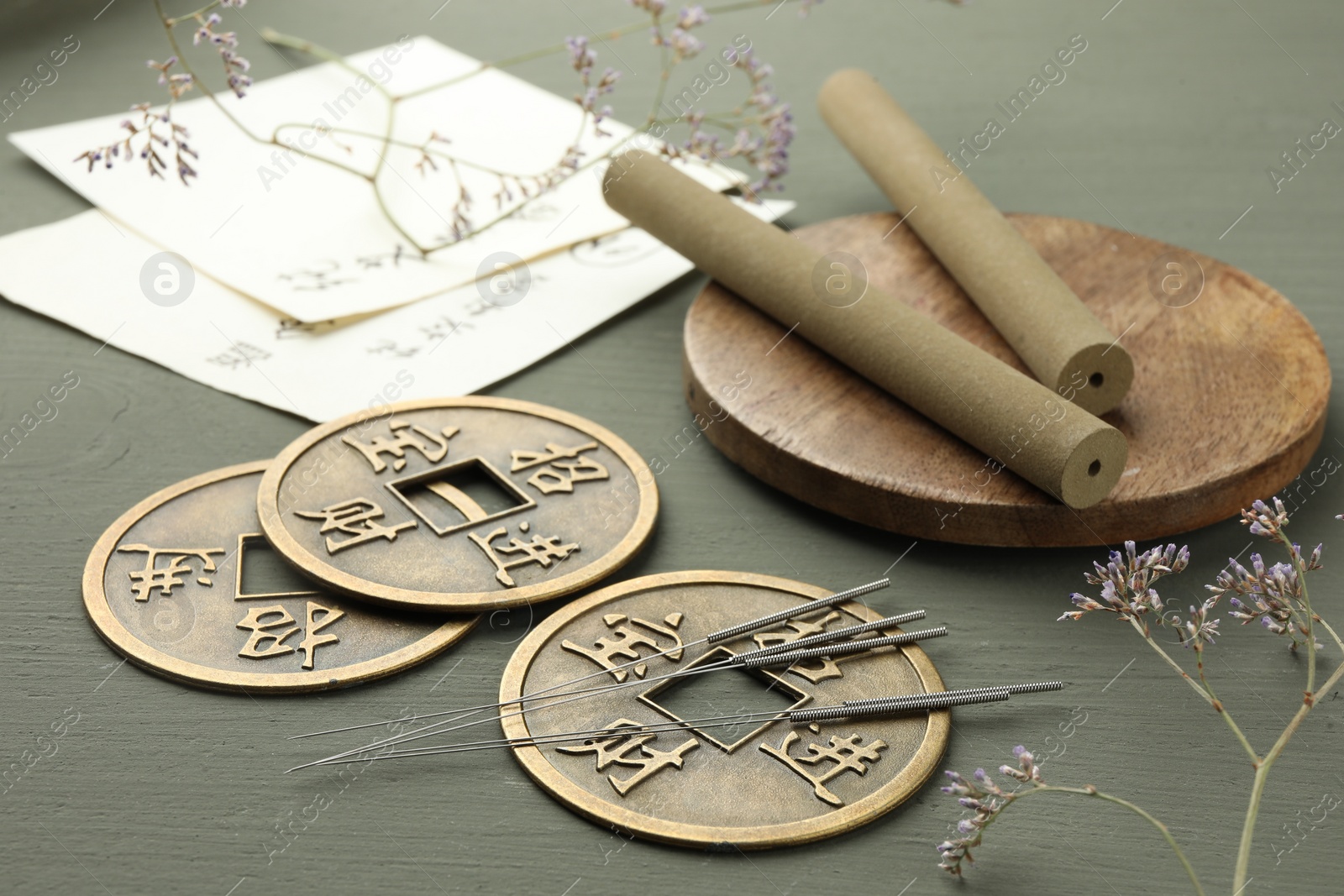 Photo of Acupuncture needles, moxa sticks and antique Chinese coins on grey wooden table, closeup