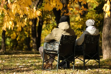 Couple sitting in camping chairs outdoors on autumn sunny day