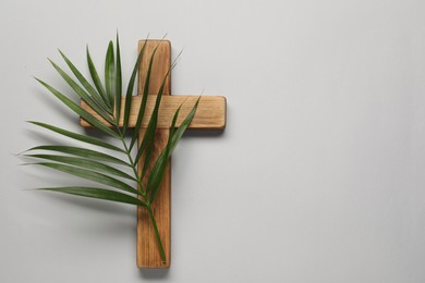 Photo of Wooden cross and palm leaf on light grey background, top view with space for text. Easter attributes