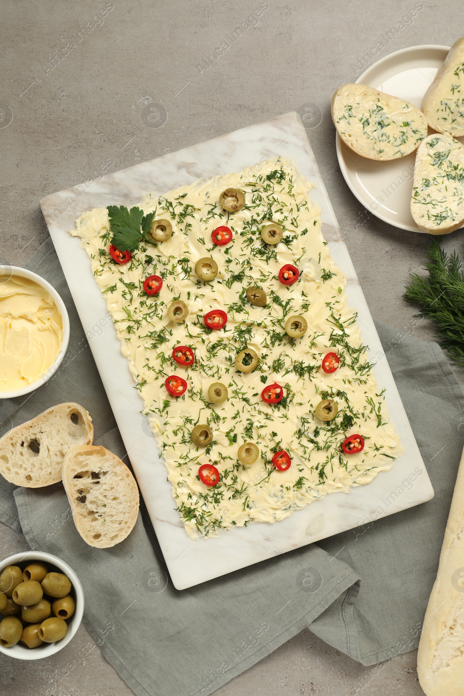 Photo of Fresh butter board with cut olives, pepper and bread on grey table, flat lay