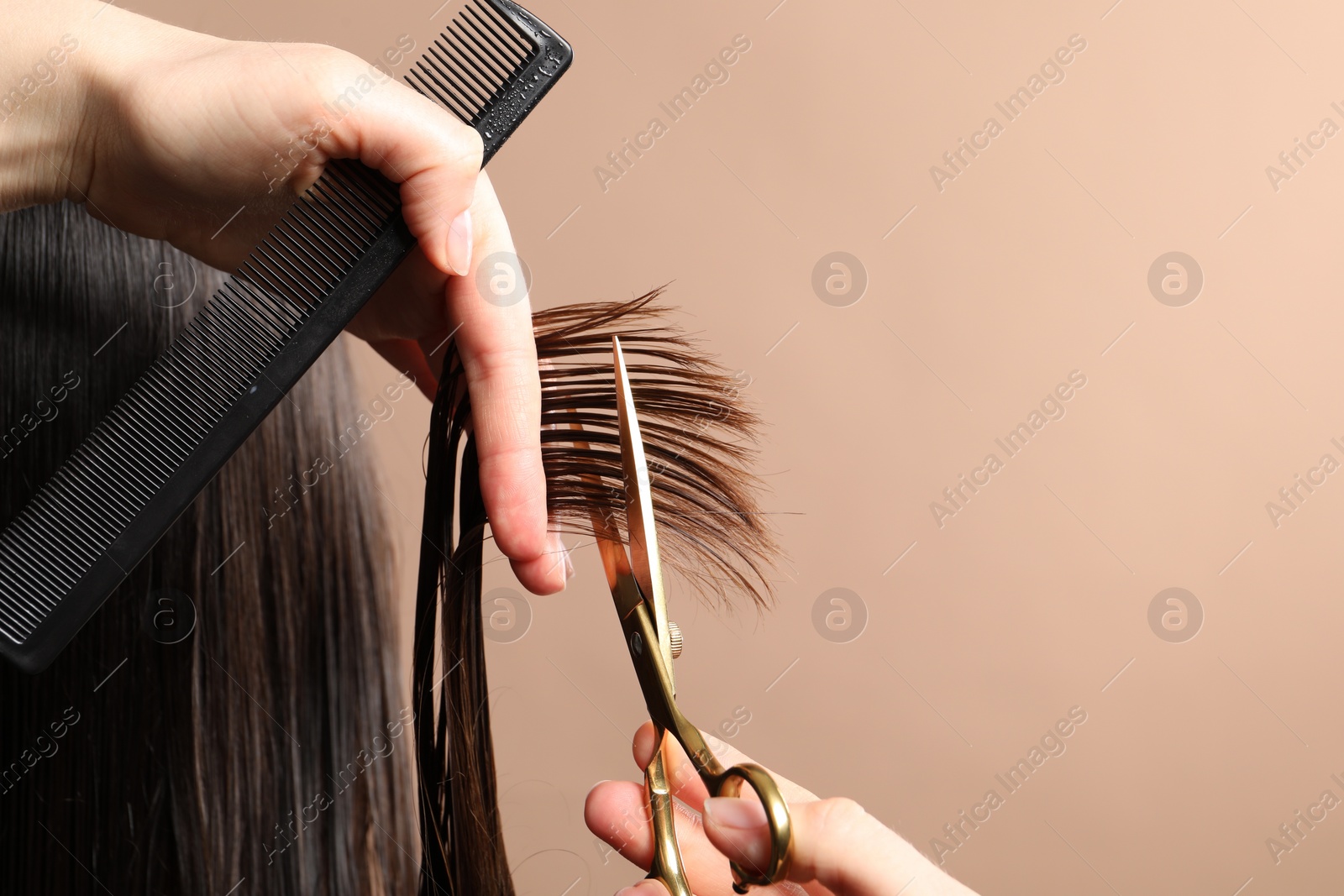 Photo of Hairdresser cutting client's hair with scissors on light brown background, closeup. Space for text