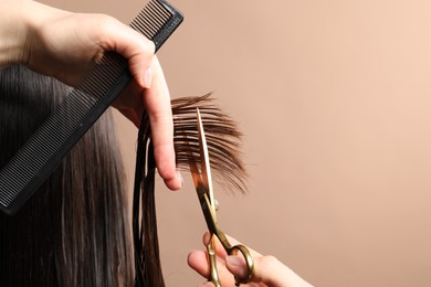 Photo of Hairdresser cutting client's hair with scissors on light brown background, closeup. Space for text