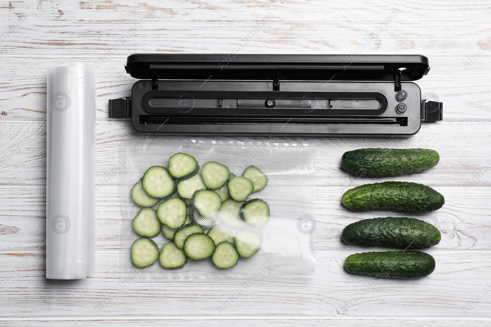 Photo of Sealer for vacuum packing, plastic bags and cucumbers on white wooden table, flat lay