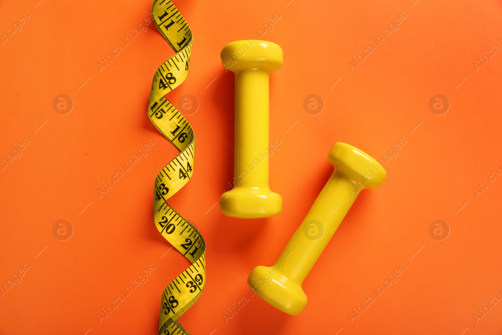 Photo of Dumbbells and measuring tape on orange background, flat lay. Weight loss concept
