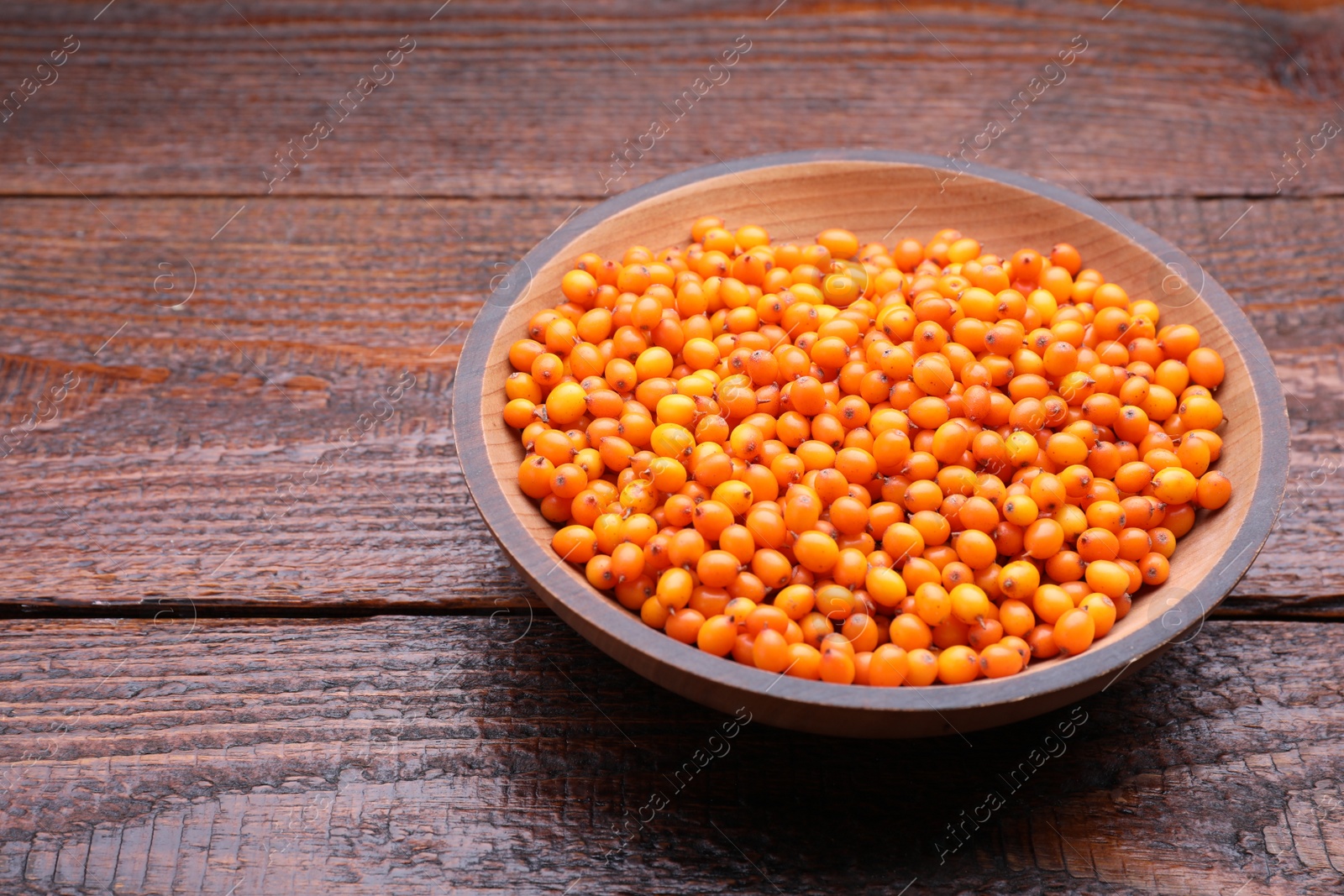 Photo of Bowl with fresh ripe sea buckthorn berries on wooden table, space for text