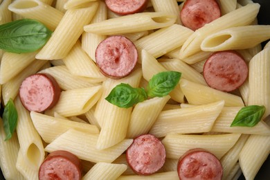 Tasty pasta with smoked sausage and basil as background, top view