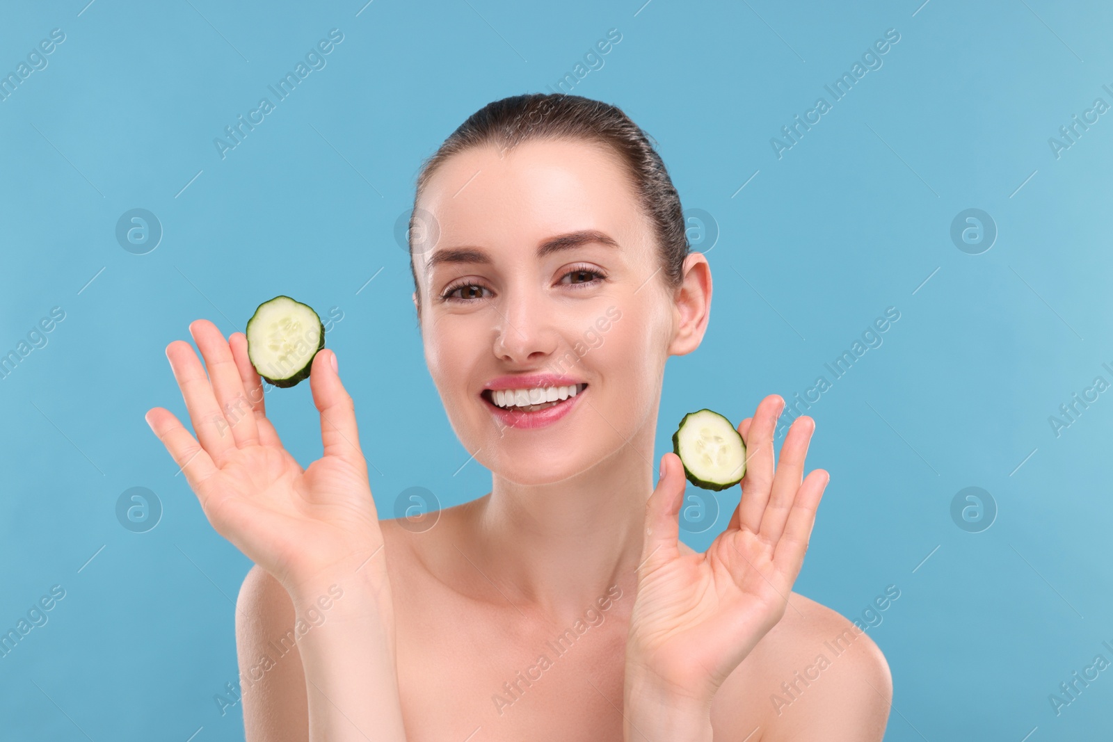 Photo of Beautiful woman with pieces of cucumber on light blue background