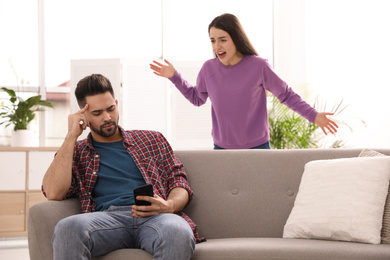 Young man with smartphone ignoring his girlfriend at home