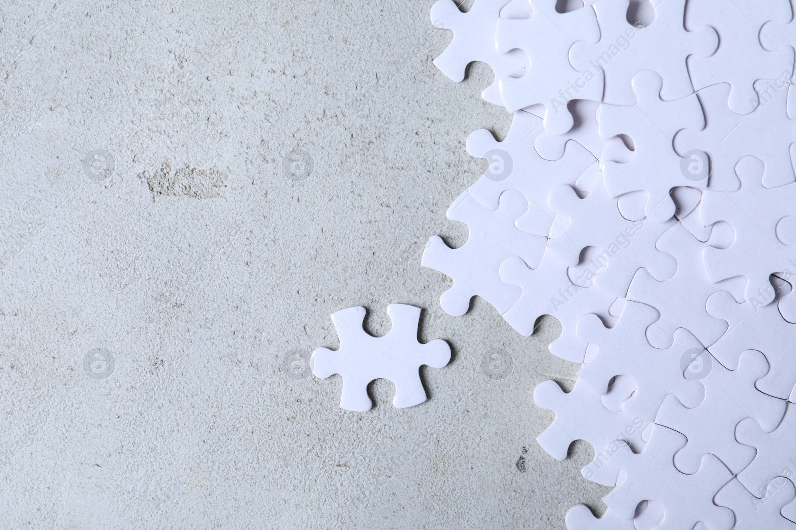 Photo of Blank white puzzle pieces on light grey stone background, flat lay. Space for text